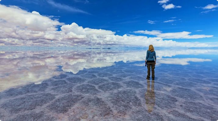 Frau blickt auf reflektierte Wolken im Salar de Uyuni, Bolivien