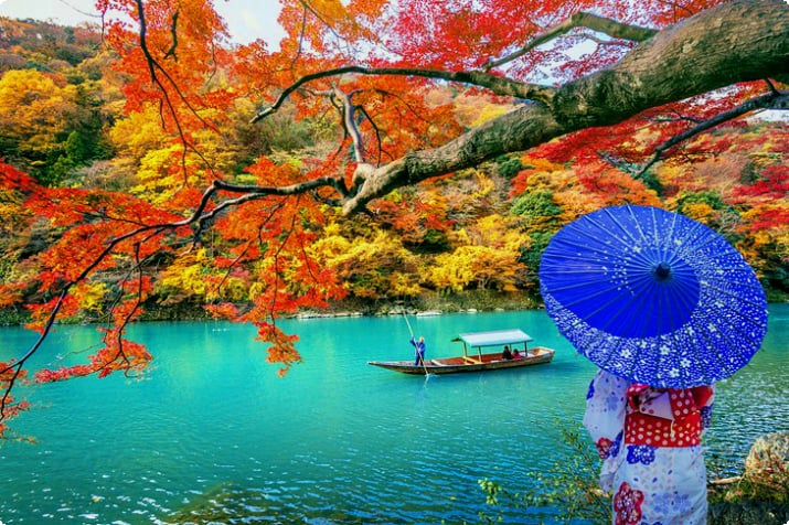 Traditionell gekleidete Frau entlang des Flusses in Kyoto mit Herbstfarben